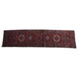 A HAND KNOTTED PERSIAN RUNNER, deep blue border on red ground with geometric motifs, 328 x 85 cm