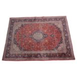 A LARGE PERSIAN HAND KNOTTED CARPET, deep blue border and central medallion on a red ground, 402 x