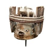 A YORUBA CARVED WOODEN HEADDRESS surmounted by a big cat in an enclosure over a stylised face.