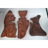Three Native American carved cedar wood wall plaques depicting a thunder bird, a salmon and a wolf,