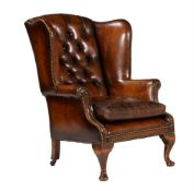 A walnut and leather buttoned wing armchair in George II style