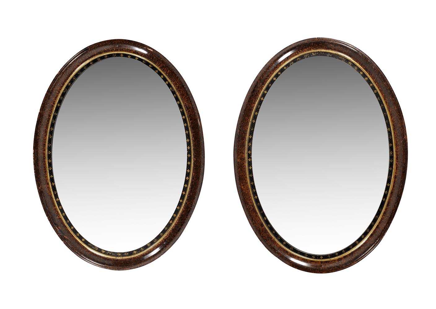 A pair of scumble framed, ebonised and parcel gilt slipped oval wall mirrors