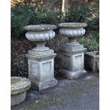 A pair of stone composition garden urns on plinths