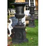 A pair of black painted cast iron campana urns on plinths