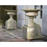 A PAIR OF REGENCY CARVED COTSWOLD STONE URNS ON PLINTH BASES, EARLY 19TH CENTURY