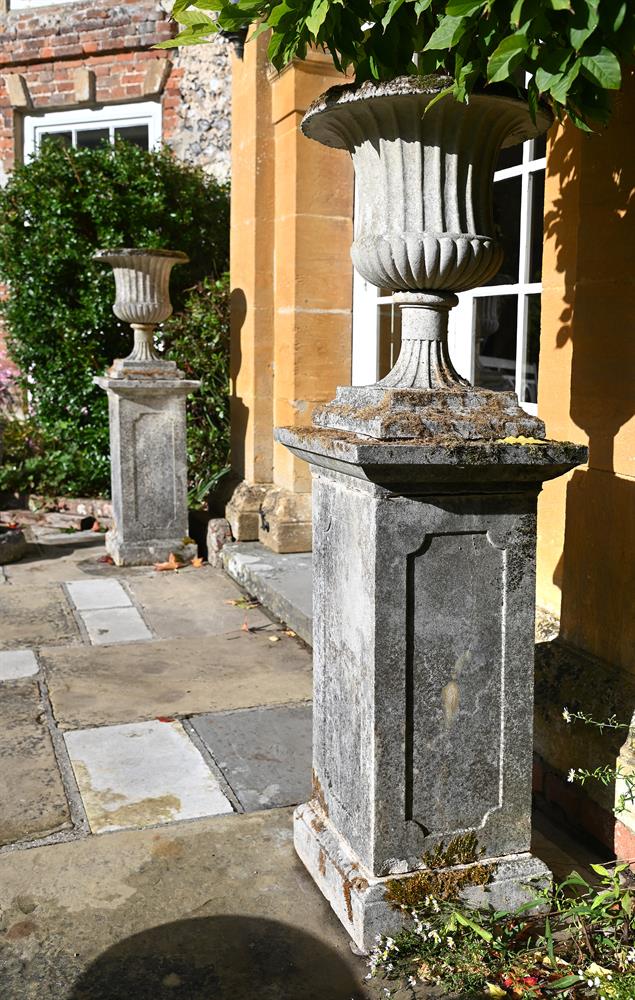 A PAIR OF COMPOSITION STONE CAMPANA URNS ON PLINTHS, LATE 19TH/EARLY 20TH CENTURY