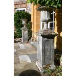 A PAIR OF COMPOSITION STONE CAMPANA URNS ON PLINTHS, LATE 19TH/EARLY 20TH CENTURY