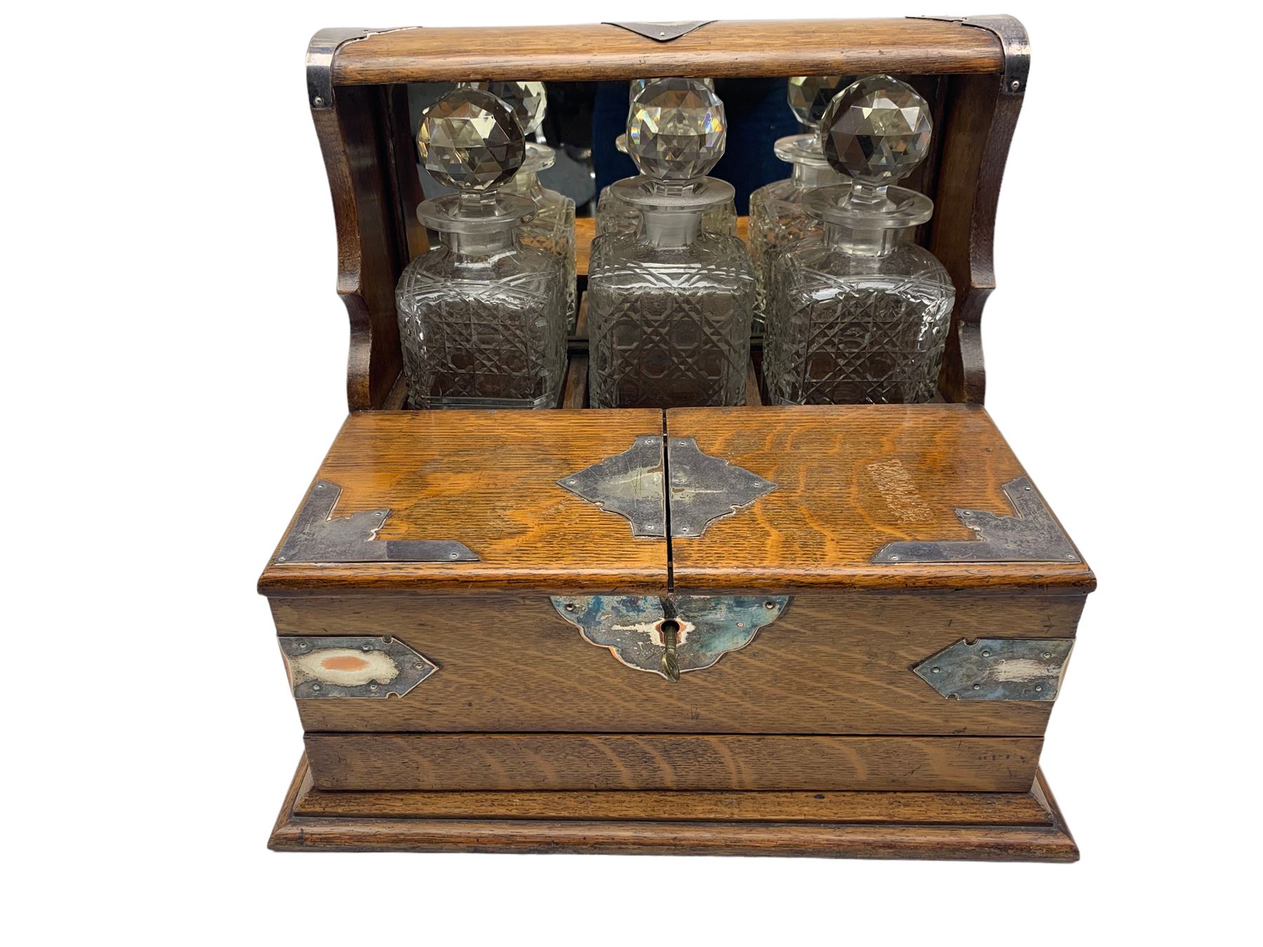 Edwardian oak three-bottle tantalus with silver-plated strapwork mounts