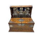 Edwardian oak three-bottle tantalus with silver-plated strapwork mounts