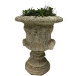 Reconstituted stone garden urn with foliate decoration and bearded masks raised on base with floral