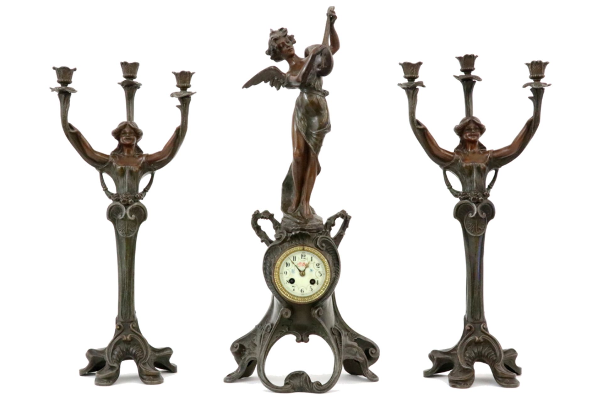 Art Nouveau garniture in zamac with several patinas : a pair of candelabra and a clock || Driedelige