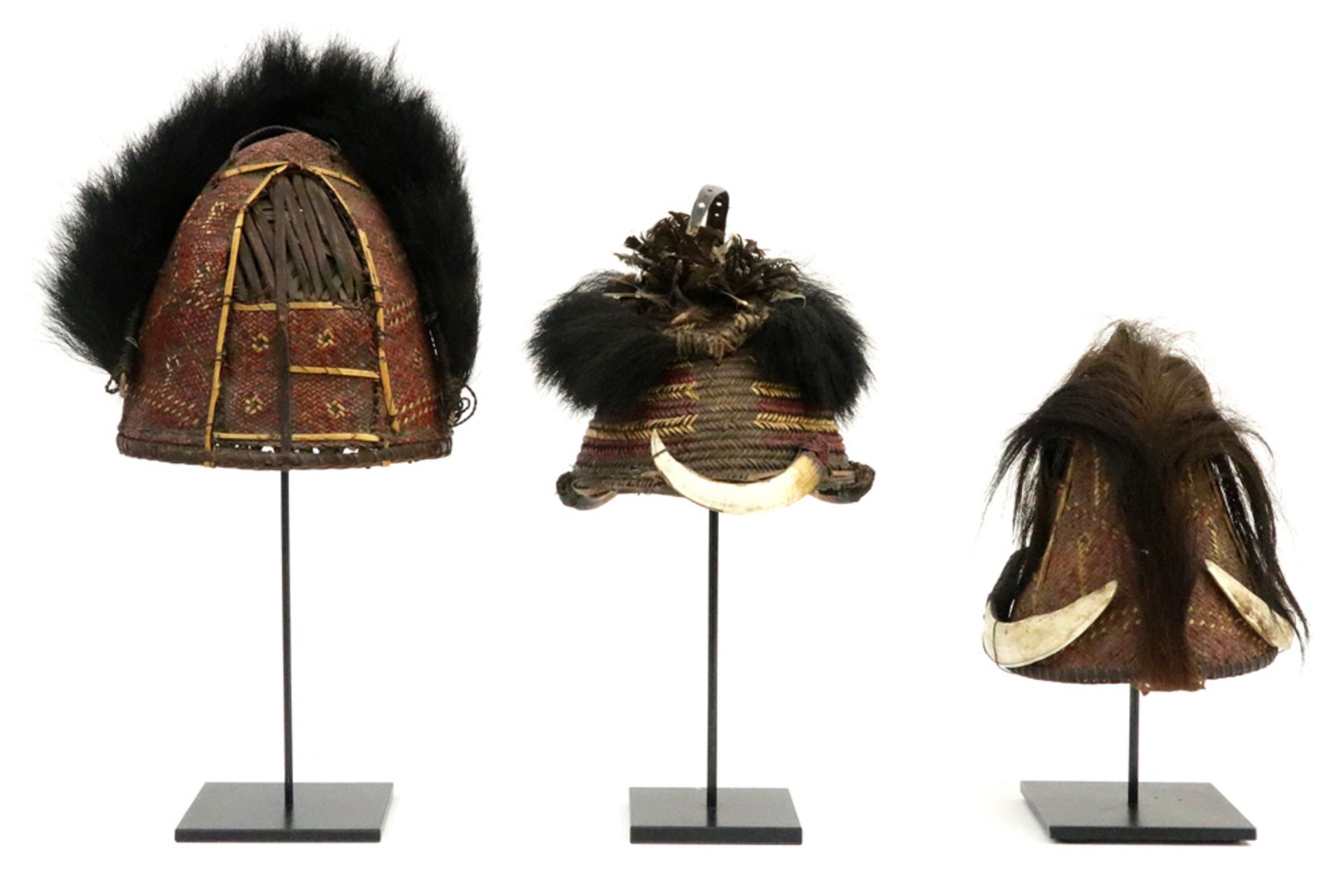 three oriental tribal hats each with tress work and with hair, feathers and/or pig's teeth || Lot