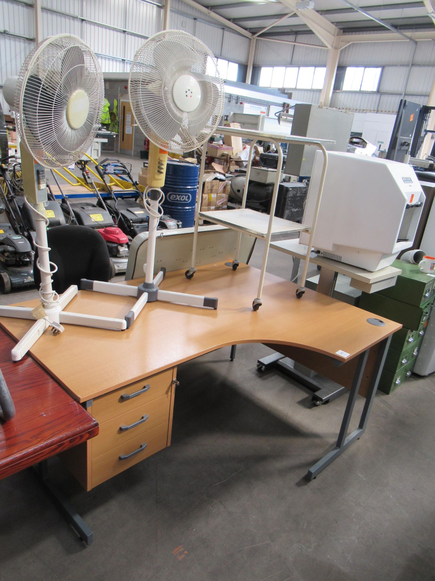 Corner left sided office desk, two fans and a mobile trolley.
