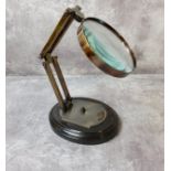 A reproduction opticians counter brass magnifying glass, articulated and mounted on wood plinth,