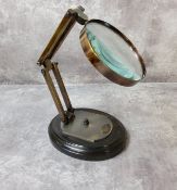 A reproduction opticians counter brass magnifying glass, articulated and mounted on wood plinth,