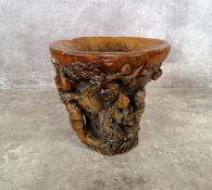 A Chinese 'rhinoceros horn' libation cup carved with immortals beneath a flowering prunus tree on