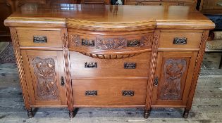 An early 20th century oak bow fronted breakfront sideboard with oversized Art Nouveau escutcheons