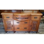 An early 20th century oak bow fronted breakfront sideboard with oversized Art Nouveau escutcheons