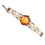 AN ANTIQUE CITRINE BANGLE in 9ct yellow gold, the tapering, hinged body with scrolling accents,