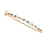 A SAPPHIRE AND DIAMOND BANGLE in 18ct yellow gold, set with a row of alternating round cut sapphires