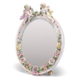 A 19TH CENTURY CONTINENTAL PORCELAIN MIRROR, the floral-encrusted frame surmounted by putti