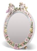 A 19TH CENTURY CONTINENTAL PORCELAIN MIRROR, the floral-encrusted frame surmounted by putti