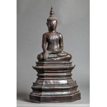 Buddha Maravijaya assis sur un haut socle étagé, les jambes en virasana et la main droite en