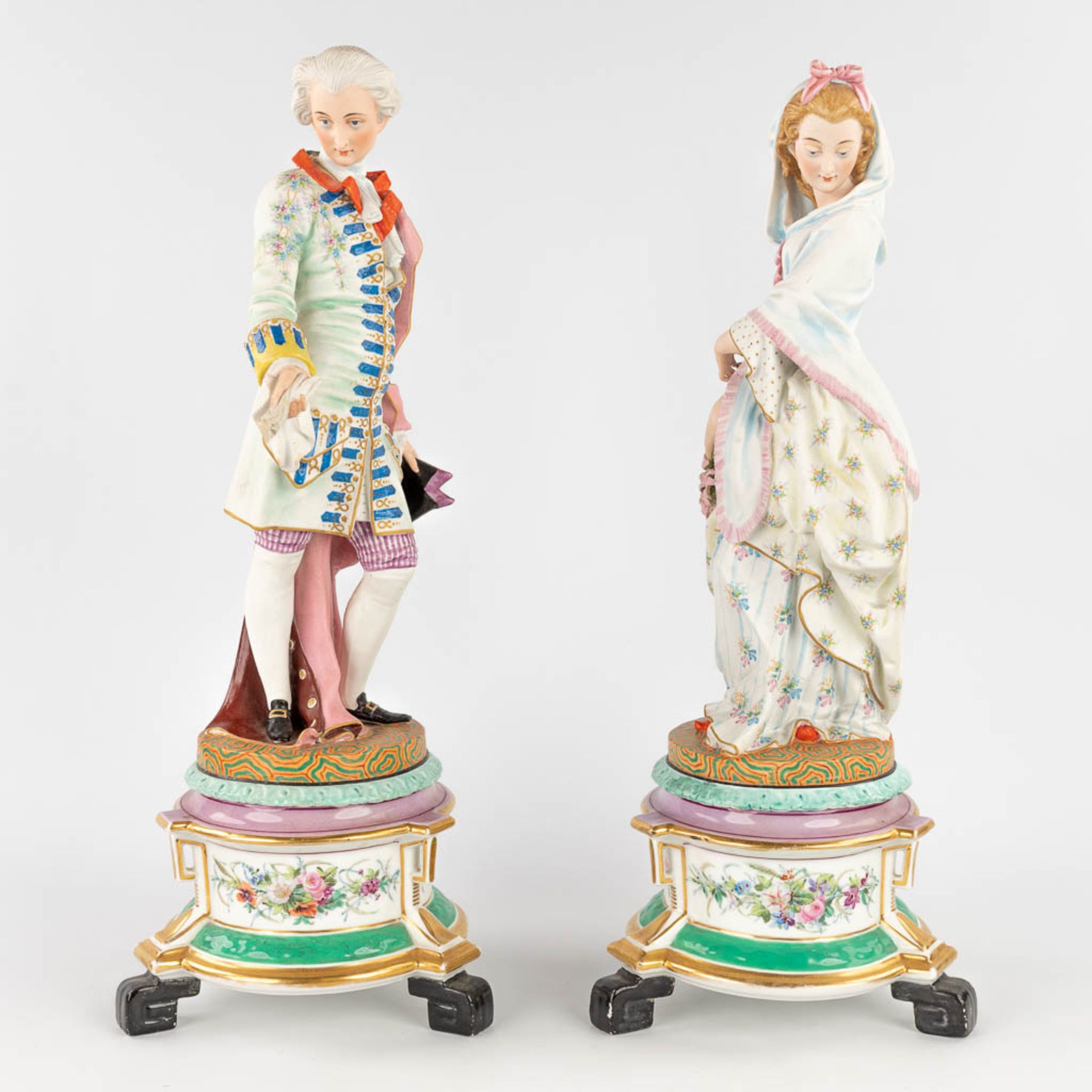 A pair of antique bisque figurines, standing on a glazed porcelain base. (L: 18 x W: 18 x H: 49 cm)