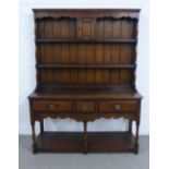 Dark oak dresser, with a wavy top over the planked back, fitted with a small cupboard and shelves