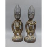 A pair of Nigerian Ibeji carved wood and bead figures, each modelled standing with their hands at