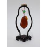 Chinese amber coloured hardstone, carved with a figure and suspended within a stylised wooden