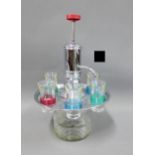 Vintage chrome and glass shot dispenser containing a set of six harlequin coloured glasses, 32cm