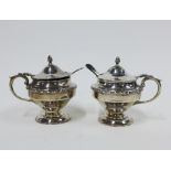 A pair of George V silver mustard condiments with blue glass liners, pair of plated salt spoons,