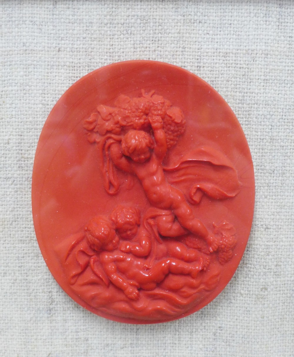 Red wax plaque of cherubs playing, framed with a glazed show frame, James McClure label verso,