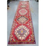 Kazak style runner, red field with five medallions and flowerhead borders, 424 x 113cm