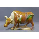 Tang style pottery figure of a bull, amber glazed with green highlights, on a shaped base, 30cm long