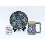 A group of Iznik style pottery to include a plate, tankard and small mug (3) 19cm.