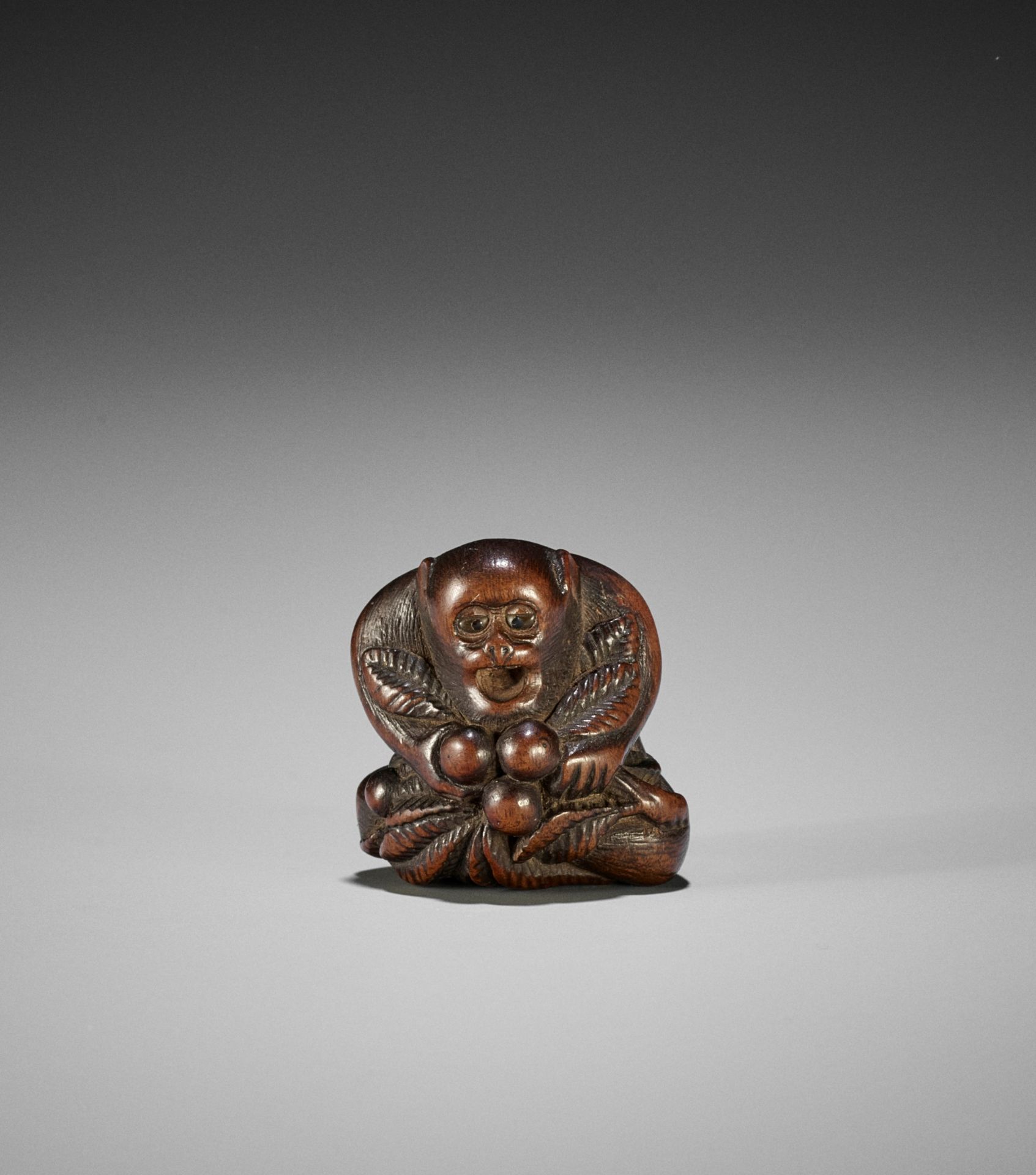 GYOKUZAN: A WOOD NETSUKE OF A MONKEY WITH BIWA (LOQUATS)