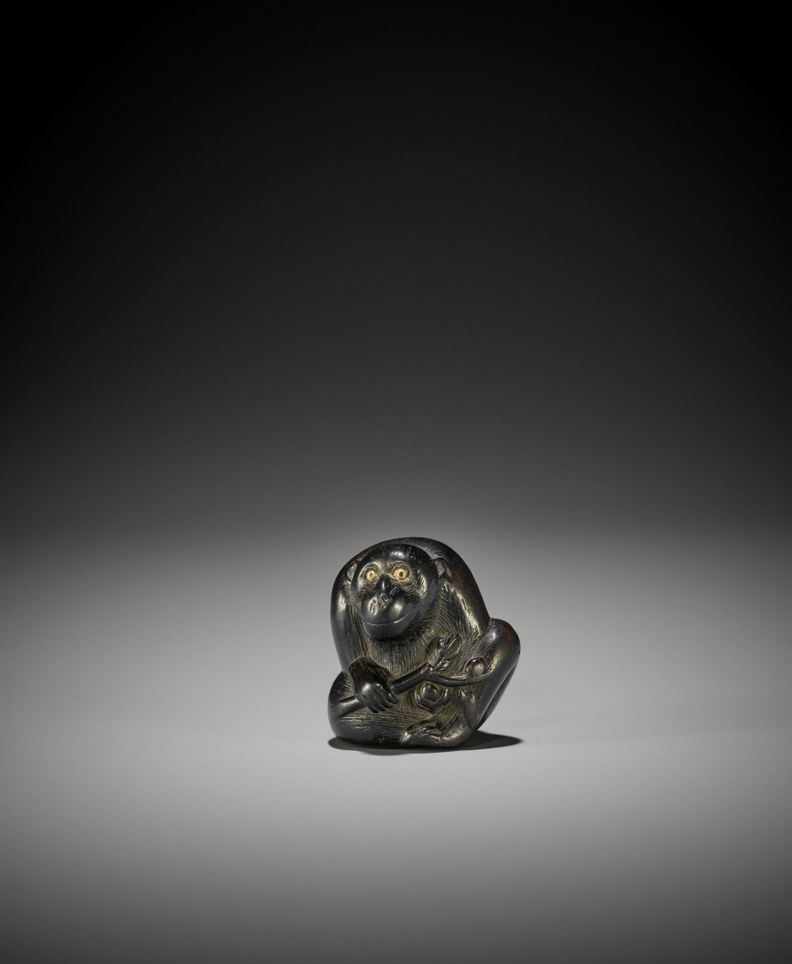 A TSU SCHOOL EBONY WOOD NETSUKE OF A MONKEY