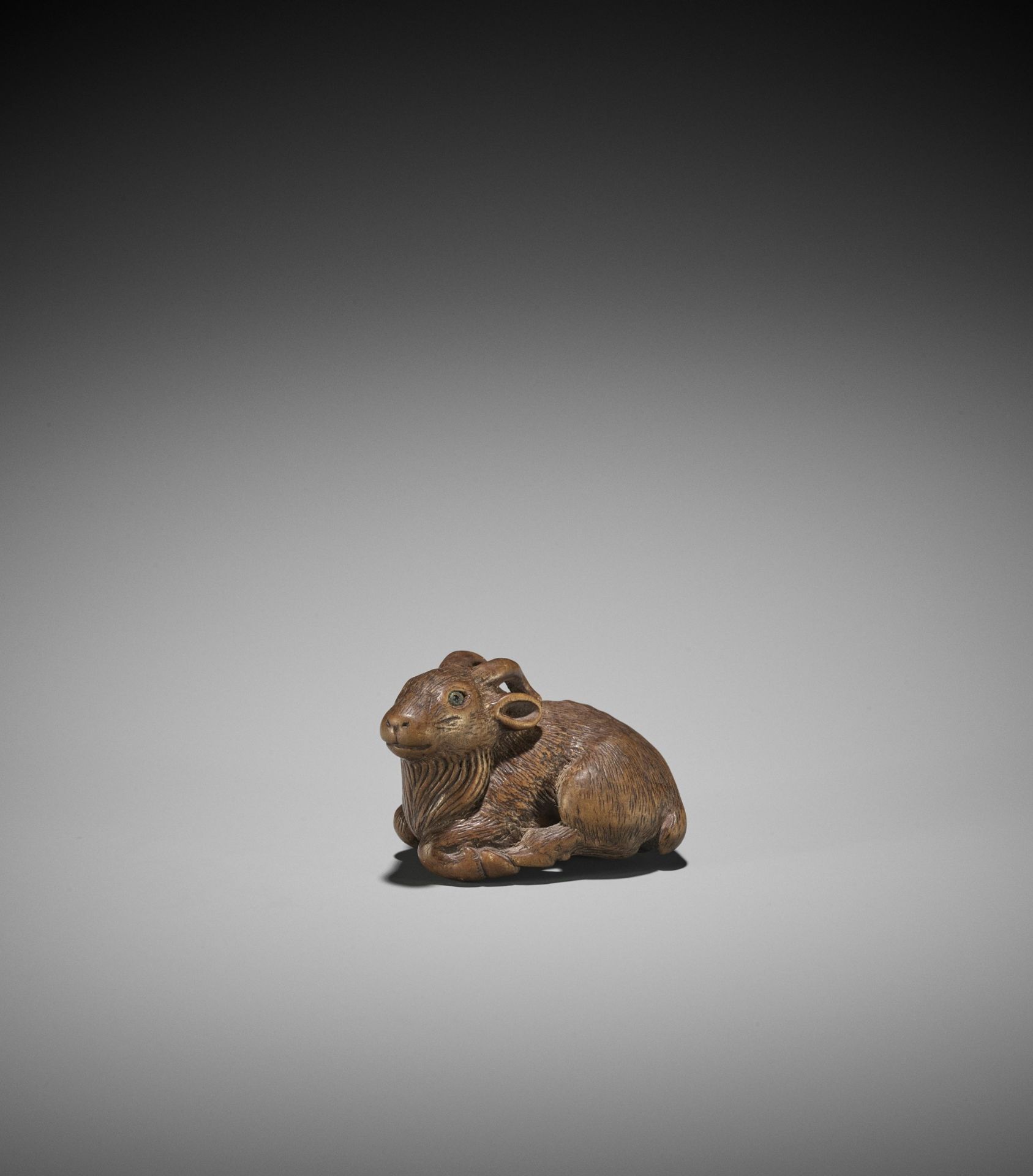 MINKO: A WOOD NETSUKE OF A RECUMBENT GOAT