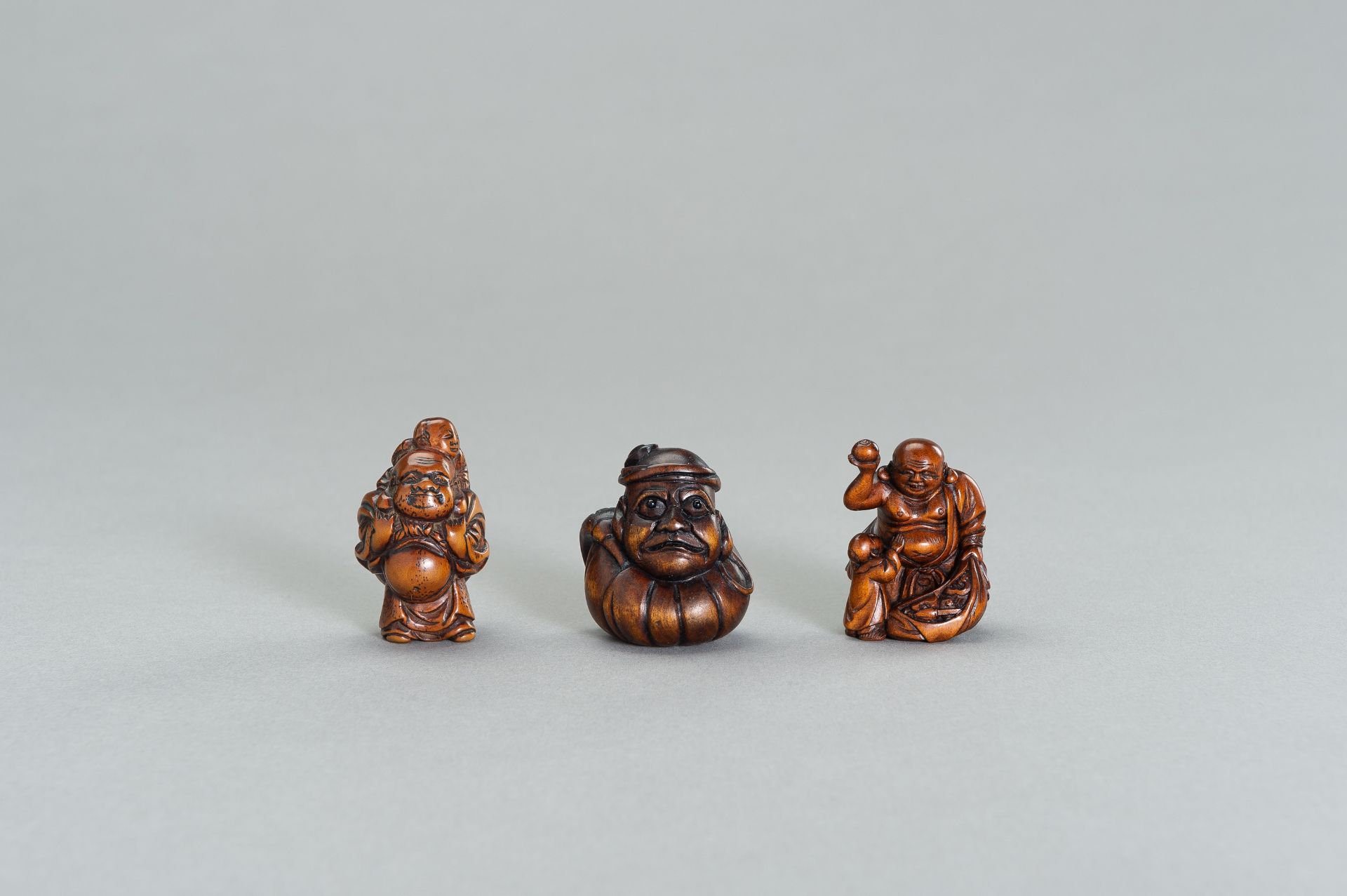 A GROUP OF THREE WOOD NETSUKE OF HOTEI AND DARUMA