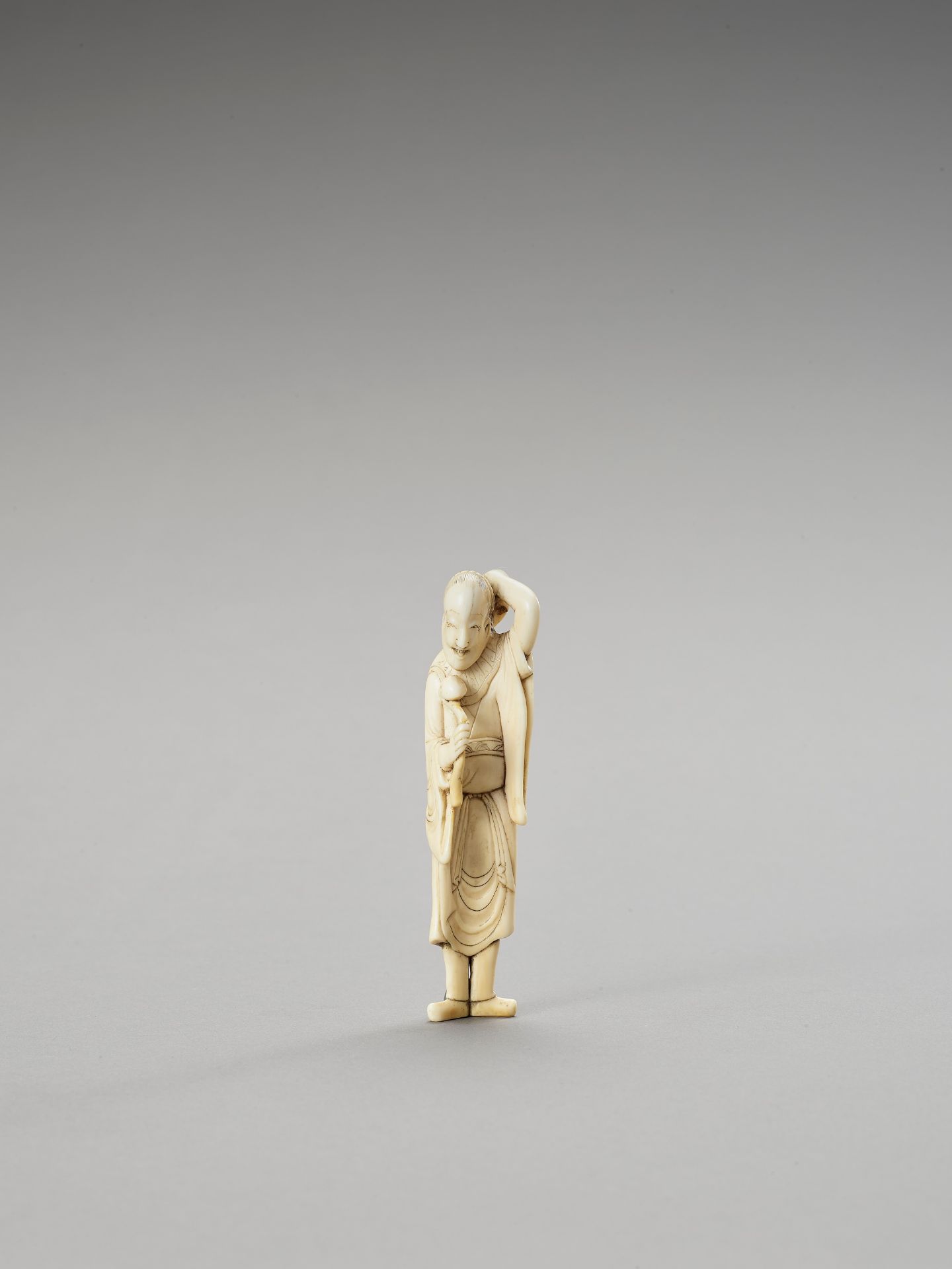 A TALL IVORY NETSUKE OF A SAGE WITH SCEPTER AND HOSSU