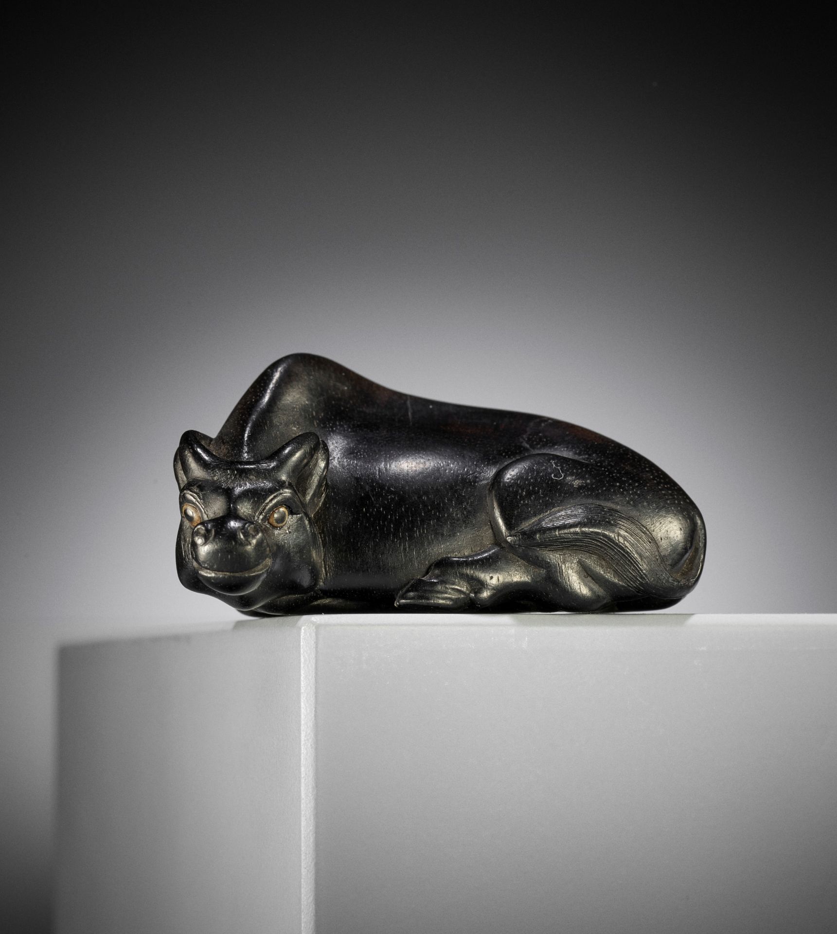 MASAYOSHI: AN EBONY NETSUKE OF A RECUMBENT OX