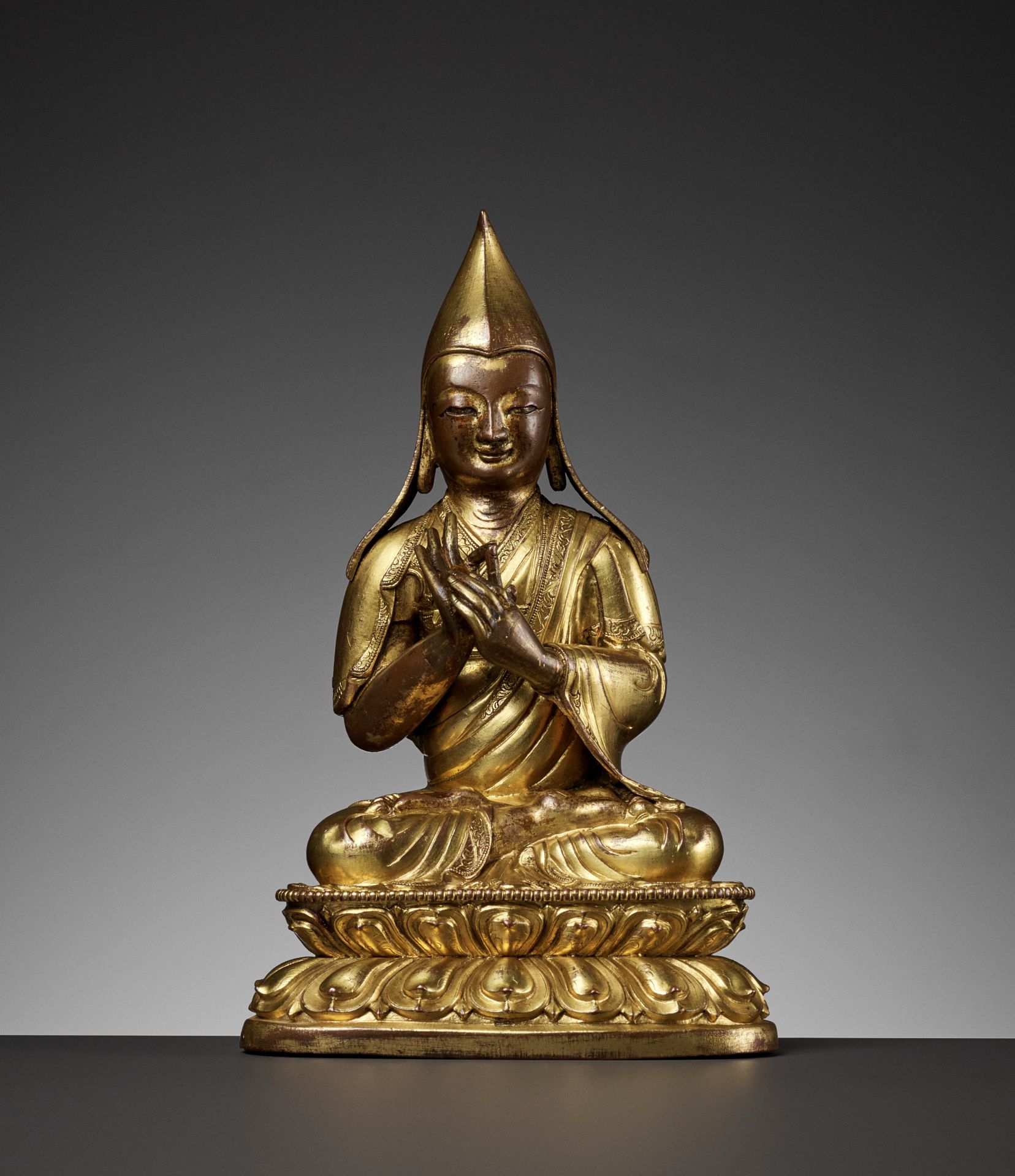 A GILT-COPPER REPOUSSE FIGURE OF A LAMA, 18TH CENTURY