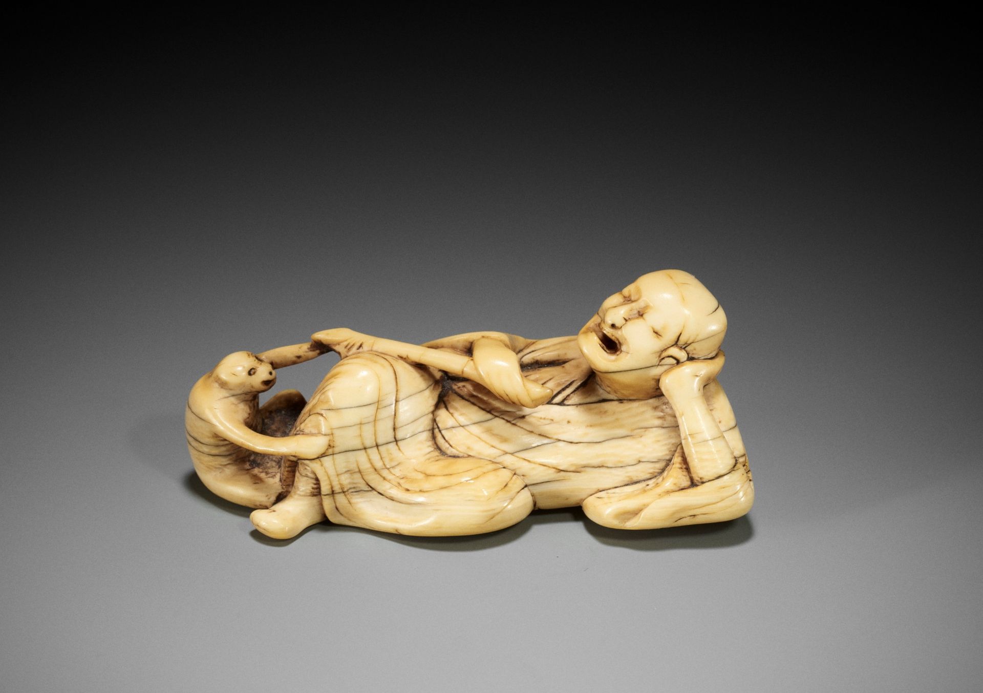 A RARE AND LARGE IVORY NETSUKE OF A RECLINING SARUMAWASHI AND HIS MONKEY