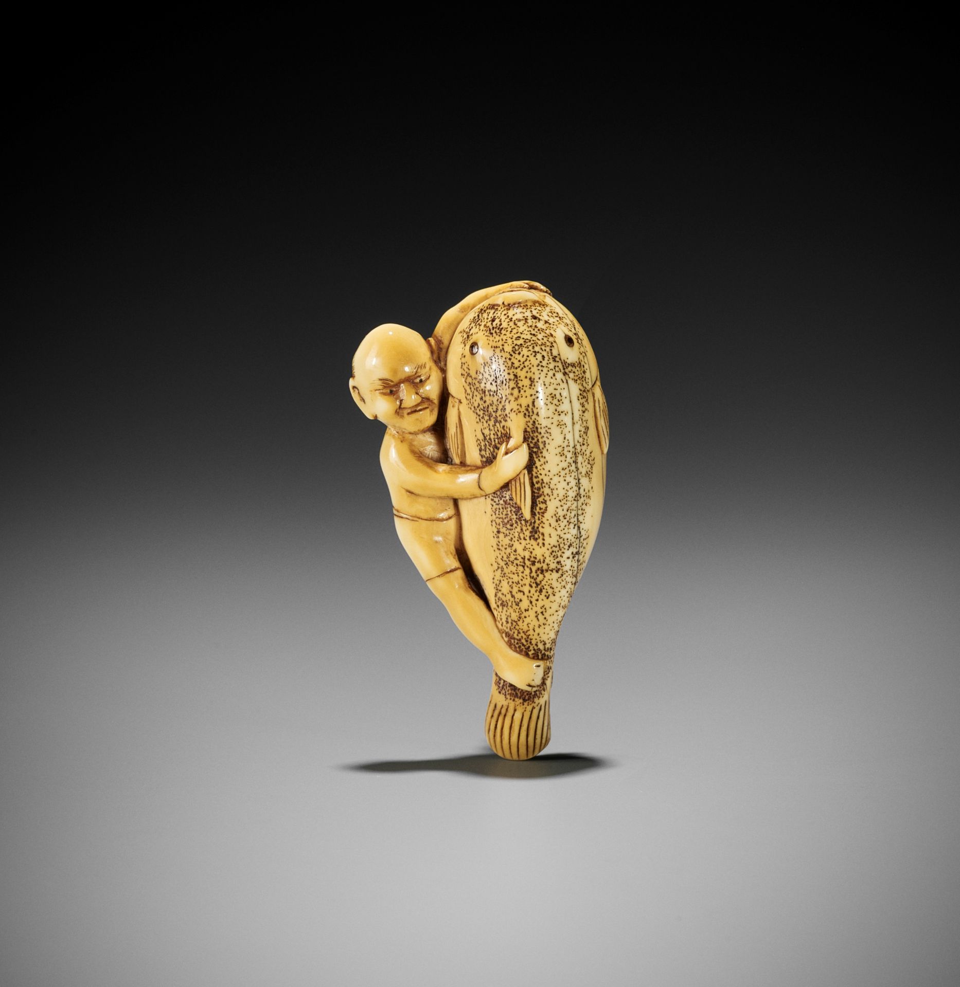 A RARE IVORY NETSUKE OF A FISHERMAN STRUGGLING WITH A GIANT FUGU