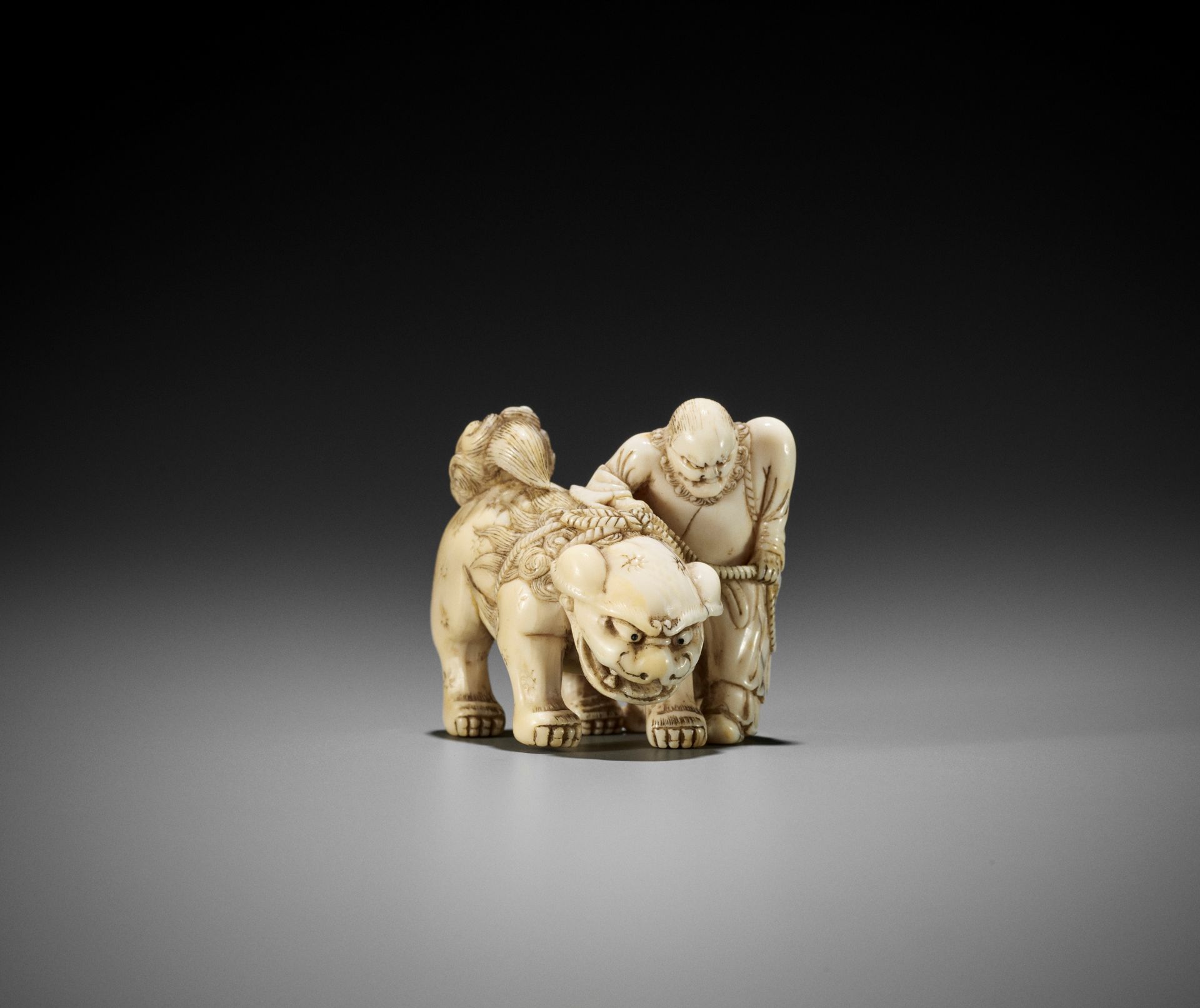 AN IVORY NETSUKE OF A FOREIGNER FROM SENHA LEADING A SHISHI