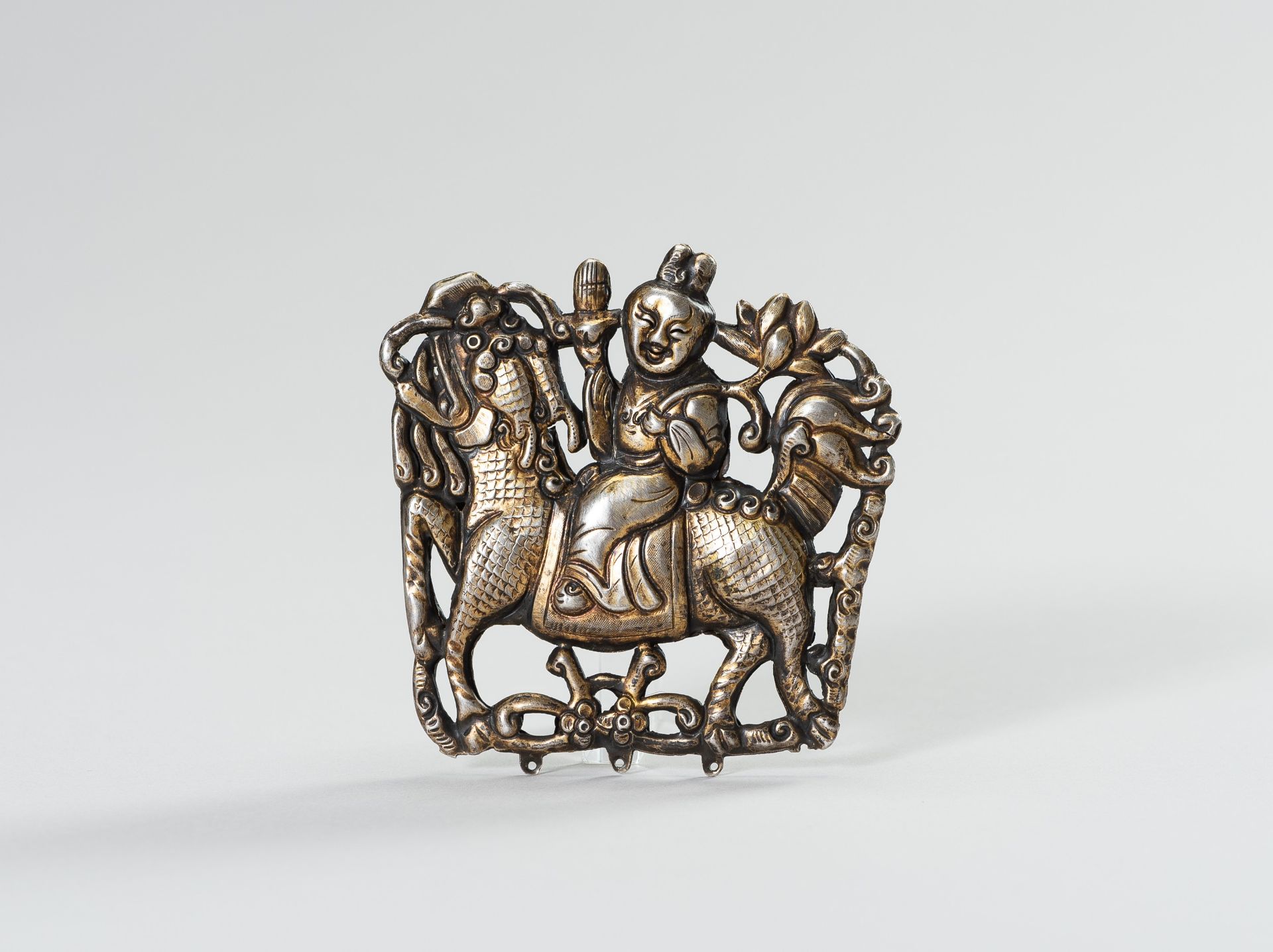 A PARCEL GILT SILVER REPOUSSE ORNAMENT OF GUANYIN ON A BUDDHIST LION