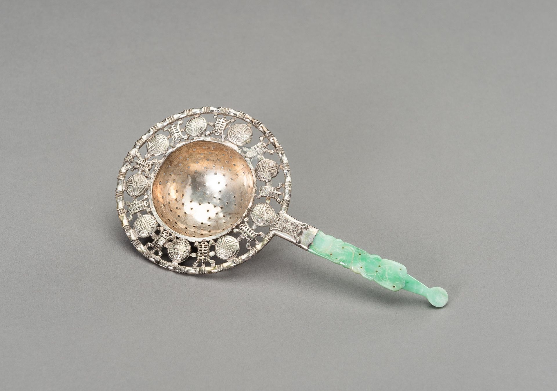 A SILVER-PLATED TEA STRAINER WITH JADEITE HANDLE