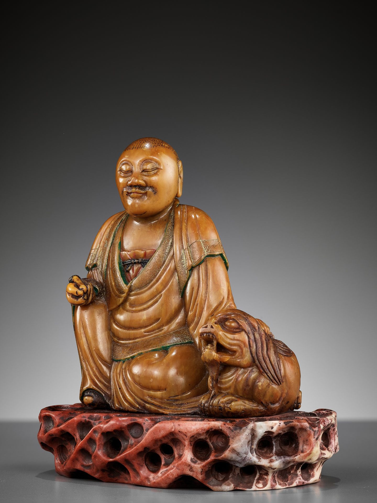 A SOAPSTONE FIGURE OF A LUOHAN WITH A BUDDHIST LION, 18TH CENTURY